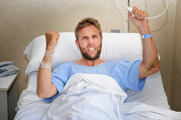 angry patient man at hospital bed pressing nurse call button stock photo