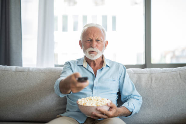 Angry senior man watching a movie at home. stock photo