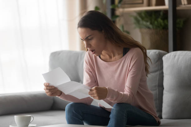 Angry woman sitting on couch holding letter received bad news Angry woman sitting on couch at home holding letter reading awful news about company job refusal feels frustrated negative emotions face expressions, college admission or bank loan rejection concept high up stock pictures, royalty-free photos & images