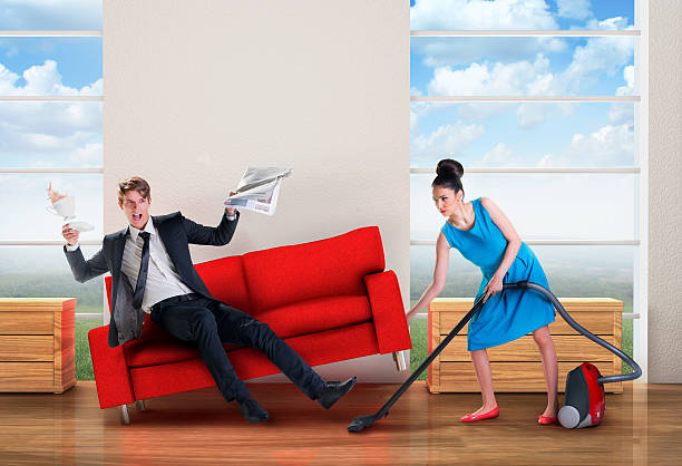 Angry woman vacuuming while man is resting stock photo