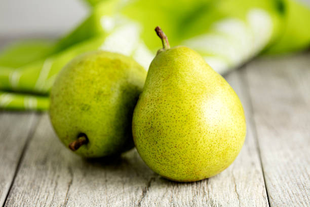 Anjou Pears Two Anjou pears sitting on a wooden table with a green tablecloth in the background pear stock pictures, royalty-free photos & images