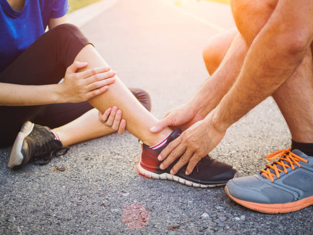Ankle sprained. Young woman suffering from an ankle injury while exercising and running and she getting help from man touching her ankle. Healthcare and sport concept. stock photo