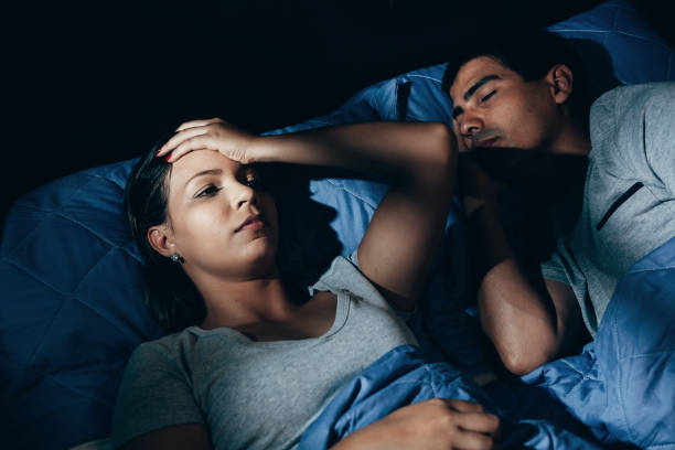 annoyed woman lying in bed with snoring boyfriend at home in the bedroom - sleeping couple imagens e fotografias de stock