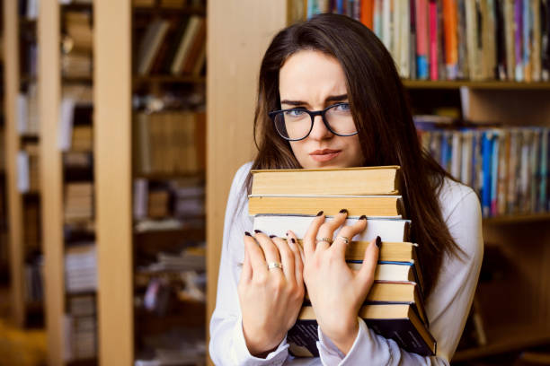 Annoyed young student woman with lots of books studying for exams in library Female student in library toughest exams stock pictures, royalty-free photos & images