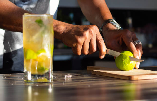 bartender châu phi vô danh cắt một lát chanh tươi để trang trí một ly cocktail mojito trong một quán bar. - frozen mojito hình ảnh sẵn có, bức ảnh & hình ảnh trả phí bản quyền một lần