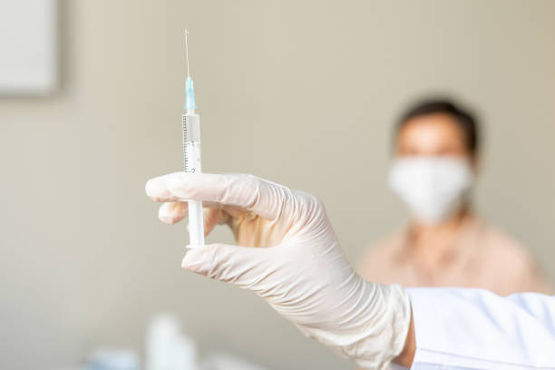 Anonymous healthcare worker vaccinating middle-aged female patient. Blurred background stock photo