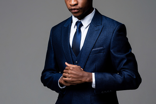 Anonymous young African man wearing formal business suit in studio gray isolated background