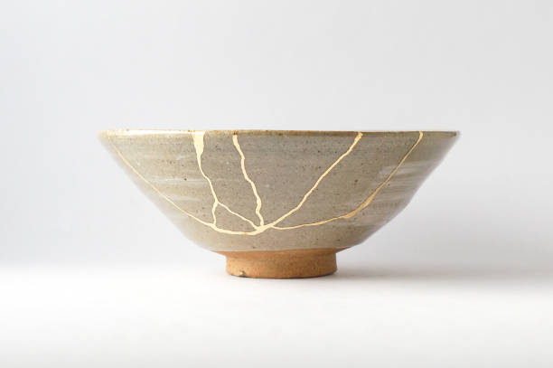 Antique broken Japanese beige bowl repaired with gold kintsugi technique Kintsugi beige bowl. Gold cracks restoration on old Japanese pottery restored with the antique Kintsugi restoration technique. The beauty of imperfections. japanese pottery repair gold. japanese art of repairing cracks with gold. japanese art of fixing broken pottery imperfection stock pictures, royalty-free photos & images