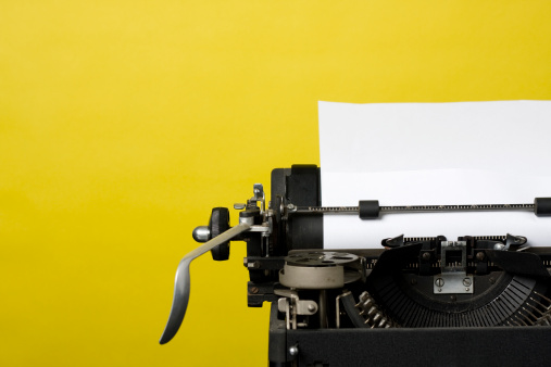 Close up shot of an antique typewriter with blank sheet of paper shot on a yellow background.