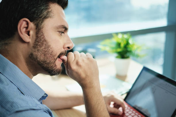 Anxious Businessman Biting Nails Working With Laptop Computer In Office stock photo