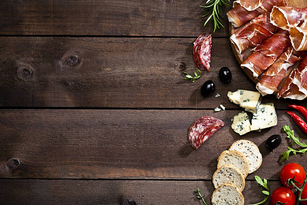 Appetizer border on rustic wood table Top view of a rustic wood table with delicatessen like prosciutto, salami, black olives, crostini, blue cheese and some herbs at the right border leaving a useful copy space.  DSRL studio photo taken with Canon EOS 5D Mk II and Canon EF 100mm f/2.8L Macro IS USM antipasto stock pictures, royalty-free photos & images