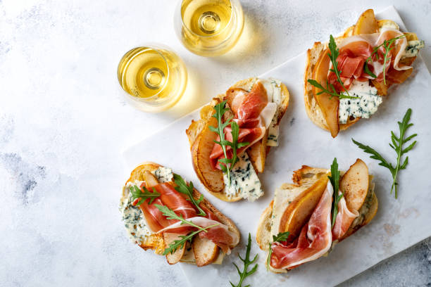 Appetizer crostini, tapas, open faced sandwiches with pear, prosciutto, arugula and blue cheese on white marble board. Delicious snack, appetizers Appetizer crostini, tapas, open faced sandwiches with pear, prosciutto, arugula and blue cheese on white marble board. Delicious snack, appetizers crostini photos stock pictures, royalty-free photos & images