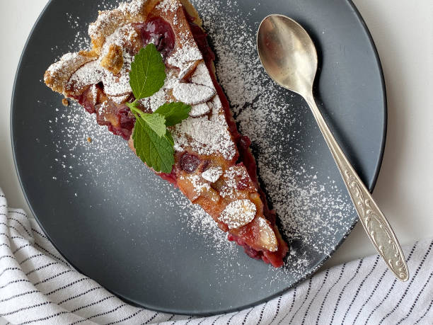 Appetizing portioned piece of cherry tart sprinkled with powdered sugar on a dark plate stock photo