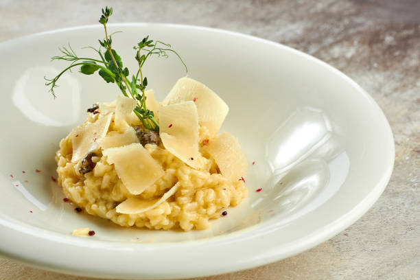 Appetizing risotto with porcini mushrooms and parmesan in a white plate on a white tablecloth stock photo