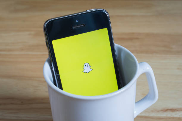 Apple iPhone5s in a mug showing its screen with Snapchat logo. stock photo