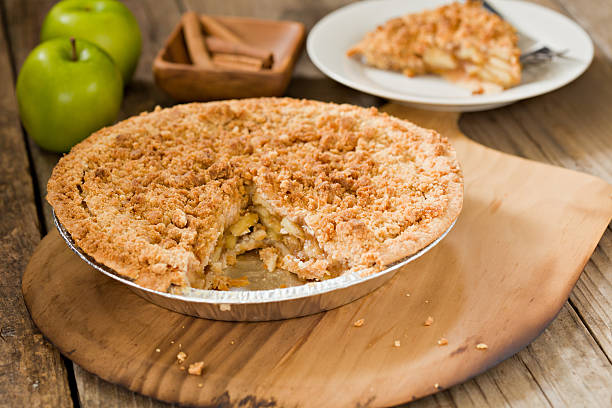 Apple Pie "A high angle close up of a dutch apple pie sitting on a wooden pizza peel, a slice of pie, cinnamon sticks and two green apples sit in the background." dutch culture stock pictures, royalty-free photos & images