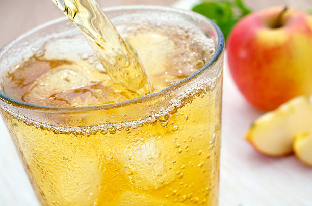 Apple spritzer pour apple juice spritzer A glass of refreshing ice-cold apple juice spritzer Apple spritzer with ice cubes is poured. The cold glass has condensed water pots. In the background is an apple and sliced apple slices.  cider stock pictures, royalty-free photos & images