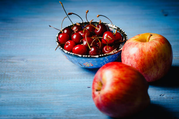 Apples and a bowl with a cherry on a blue wooden countertop