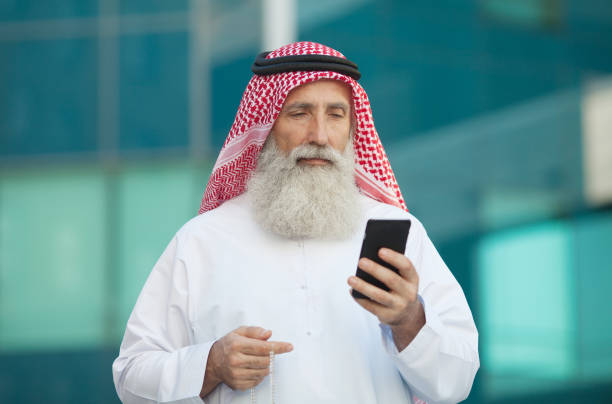 Arab businessman working with his phone. Arab businessman working with his phone on a street in the background old arab man stock pictures, royalty-free photos & images