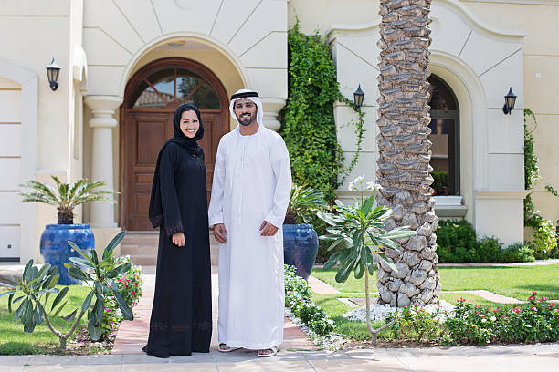 Arab family portrait in front of their house Middle Eastern couple standing in front of their house on a sunny day, both wearing the traditional Emirati dresses . middle eastern woman stock pictures, royalty-free photos & images