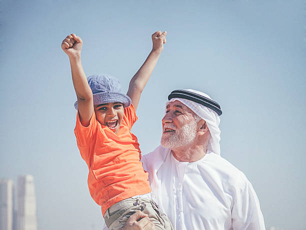 Arab grandfather and little boy having fun at beach Middle eastern grandpa and grandson enjoying on the sandy beach. old arab man stock pictures, royalty-free photos & images