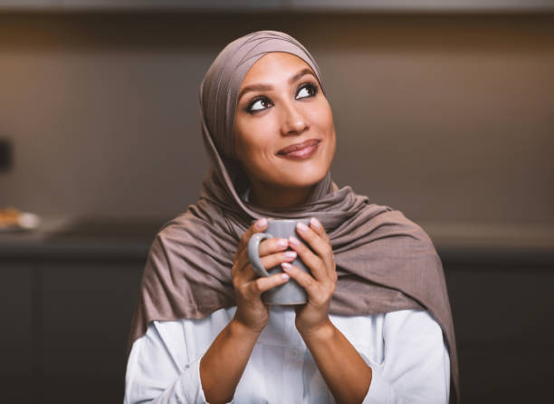Arab Lady Drinking Coffee Dreaming Looking Aside Sitting In Kitchen Muslim Woman's Dreams. Happy Arab Lady Drinking Coffee Dreaming And Thinking About Something Looking Aside Sitting In Modern Kitchen At Home, Wearing Hijab. Cozy Weekend Evening Concept hot arab woman stock pictures, royalty-free photos & images