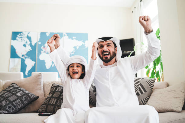 Arab man looking TV at home during a sport event with his son Arab man looking TV at home during a sport event with his son agal stock pictures, royalty-free photos & images