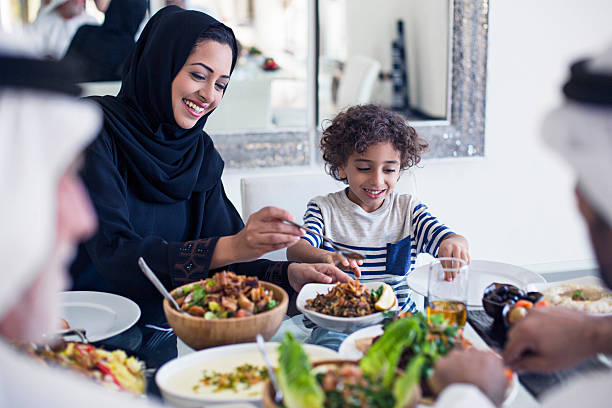 Arabic lunch time Middle Eastern family eating lunch at home, mother is serving to her son. abaya clothing stock pictures, royalty-free photos & images