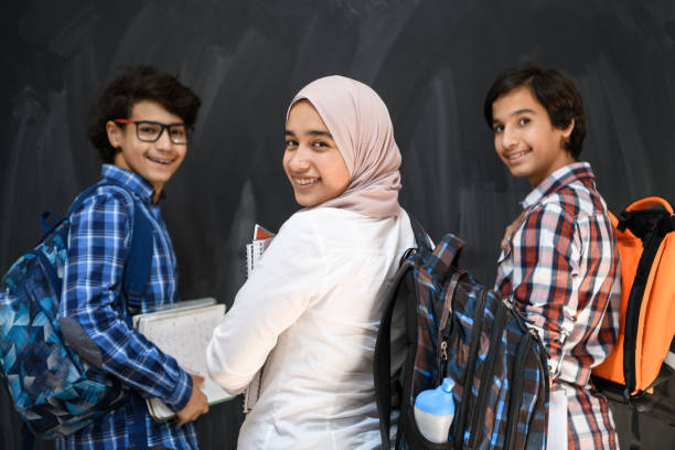 Arabic teenagers, students group portrait against black chalkboard wearing backpack and books in school.Selective focus stock photo