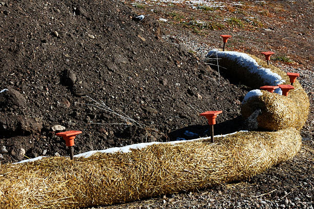 Arc of Fiber Rolls keeping black soil from eroding Construction material where straw is stuffed into netting to use for erosion control.   Here there is a pile of black soil surrounded by two fiber rolls which have been staked into place using metal rods with orange plastic caps.  Construction sites often need to temporarily store materials like this dirt and ensure it is not washed away by rainfall. erosion control stock pictures, royalty-free photos & images