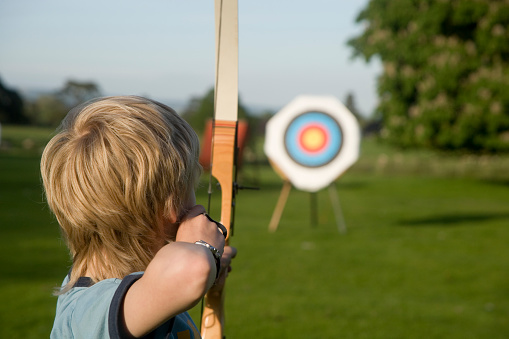 Boy taking part in the sporting activity of archery.  Taking aim at the target