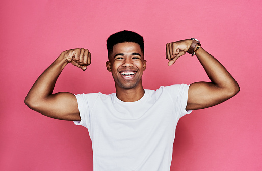Cropped portrait of a handsome young man standing alone and flexing his biceps against a pink background in the studio