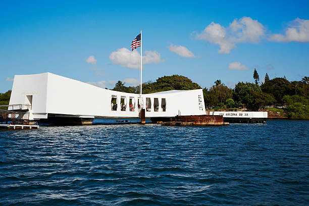 USS Arizona Memorial, Pearl Harbor, Hawaii Pearl Harbor, Hawaii, USA -- April 26, 2013: The USS Arizona Memorial in Pearl Harbor in Oahu, Hawaii as seen from a shuttle boat arriving. Guests are visible on the memorial. Also visible is the concrete plaform identifying the remains of the USS Arizona. pearl harbor stock pictures, royalty-free photos & images