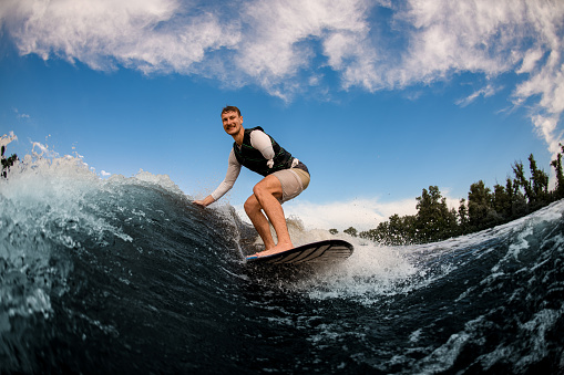 active armless man wakesurfing on the board down the wave against the background of sky. Wakesurfing on the river