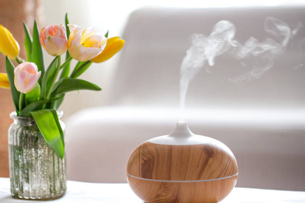 Aroma oil diffuser lamp on the table . Aroma oil diffuser lamp on the table on a blurred background with a beautiful spring bouquet of tulips. aromatherapy stock pictures, royalty-free photos & images