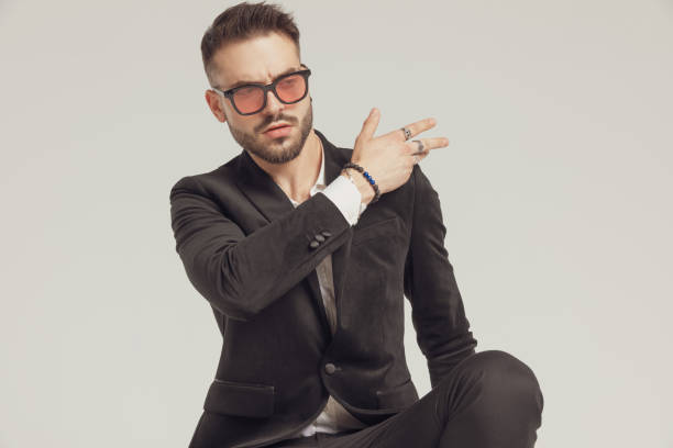 Arrogant fashion model cleaning his shoulder, wearing sunglasses Arrogant fashion model cleaning his shoulder, wearing sunglasses while crouching on gray studio background arrogance stock pictures, royalty-free photos & images