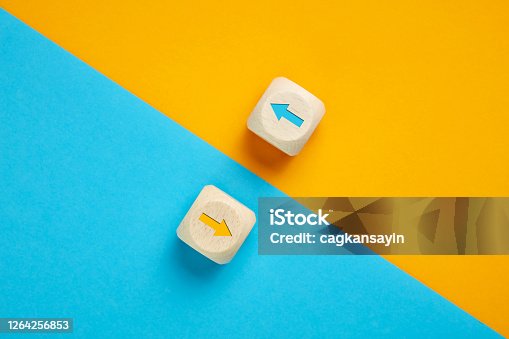 istock Arrow icons in contrast on wooden cubes moving towards opposite directions. Competition, diversity, opposition or confrontation concept. 1264256853