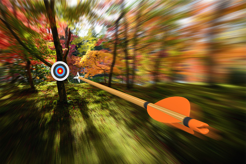 Archery concept of an arrow flying through the air at high speed toward the center of a distant target with motion blur effect. The arrow and target are rendered in 3D.