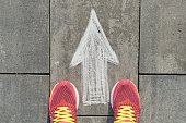 istock Arrow sign painted on gray sidewalk with women legs in sneakers, top view 1140975453