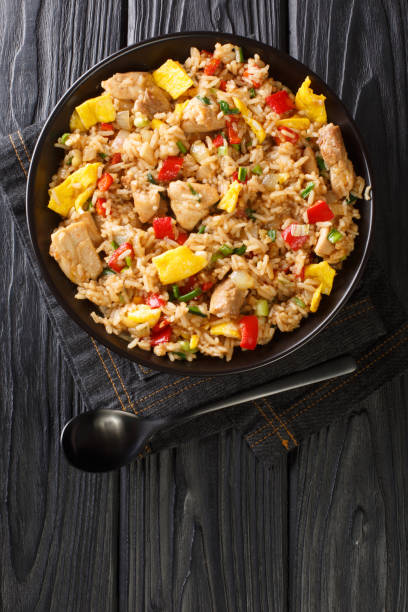Arroz Chaufa is Peruvian Chinese fried rice consists of rice, red bell peppers, onions, garlic, soy sauce, scrambled eggs and chicken close up in the bowl. Vertical top view stock photo