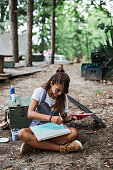 Beautiful and happy young woman enjoying in nature and summer camp. She siitting and painting in the woods.