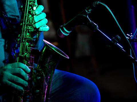 close up hands of artist musician plays the saxophone at a concert in front of the microphone illuminated by green light