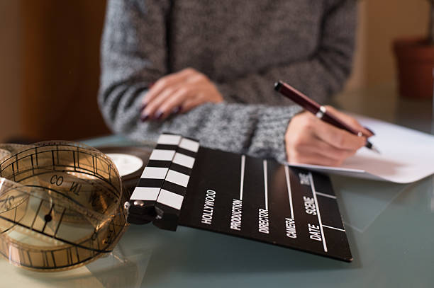 Artist screenwriter desktop detail clapper board Artist screenwriter desktop detail with movie clapper board and filmstrip with woman's hand working in background film script stock pictures, royalty-free photos & images