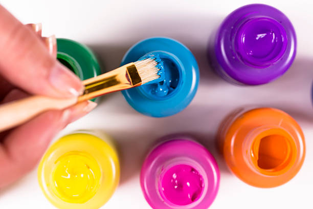 Arts and Crafts: Paintbrush with multiple colored jars. Creative hobby. Paintbrush being dipped into blue paint bottle.  Multiple colors of paint. tempera painting stock pictures, royalty-free photos & images