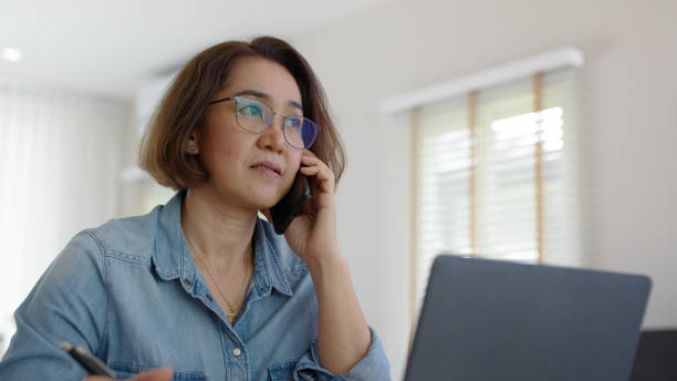 Asia adult people or SME owner woman leader moody sitting tired busy phone call work on laptop computer at desk house office think worry concern give advice on distance job crisis corporate trouble. stock photo