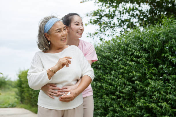 asian adult daughter hug her senior mother in backyard garden  at home . young woman embrace old mom  to take care in park outdoors. stock photo