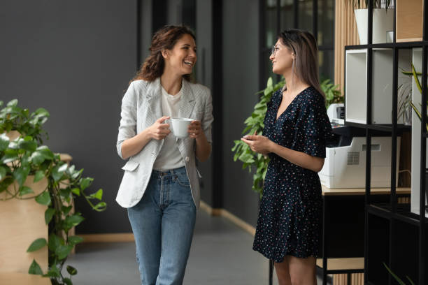 aziatische en kaukasische etniciteit vrouwen collega's chatten in de hal van het kantoor - walking with coffee stockfoto's en -beelden