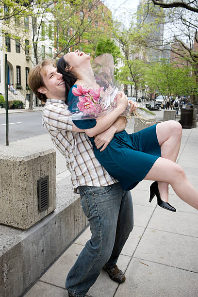Asian and Caucasian Young Couple Playing Around Outside, New York "Man hugs and lifts his date from behind, as they share a laugh together. She's holding flowers from him. Copy space below. CLICK FOR SIMILAR IMAGES AND LIGHTBOX WITH VALENTINES IMAGES." tickling beautiful women pictures stock pictures, royalty-free photos & images