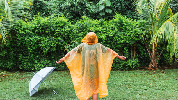 Asian boy wearing orange raincoat is happy and having fun in the rain on a rainy day. stock photo