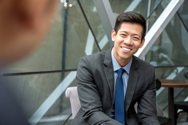 Asian businessman sitting at office lounge Friendly smiling handsome Asian businessman sitting at office lounge talking with his colleague airport terminal photos stock pictures, royalty-free photos & images